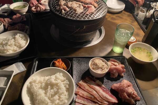 丸い炭火の焼き台に肉がのり、ご飯や汁物、生肉のトレーが並ぶ卓