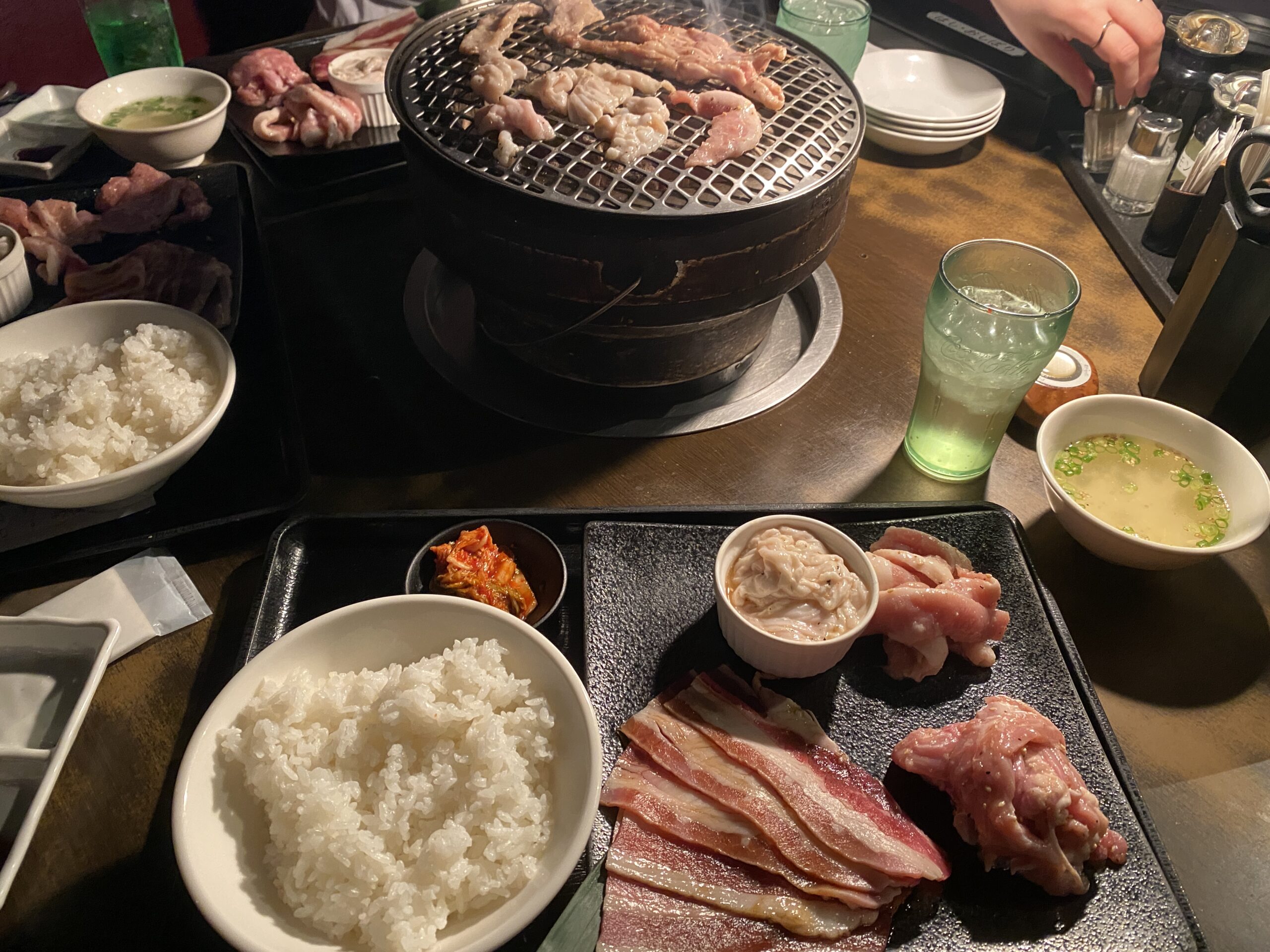 丸い炭火の焼き台に肉がのり、ご飯や汁物、生肉のトレーが並ぶ卓