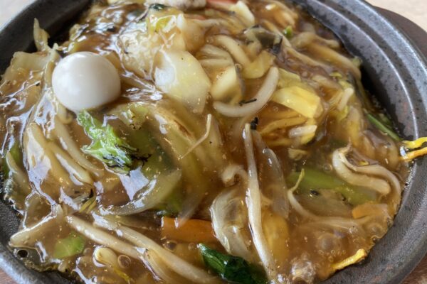 窓の外に海が広がる席に置かれた、湯気の立つあんかけ焼きそば